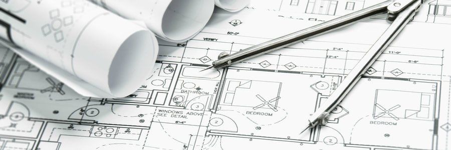 Planos con distribuciones de habitaciones, varios papeles enrollados y un compás metálico abierto sobre el papel.